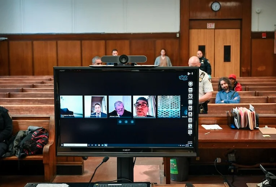 View of a courtroom with a computer screen showing a Zoom call and some attendees sitting in the room in person
