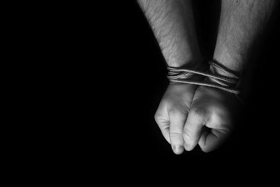 black and white image of a person's wrists bound with rope